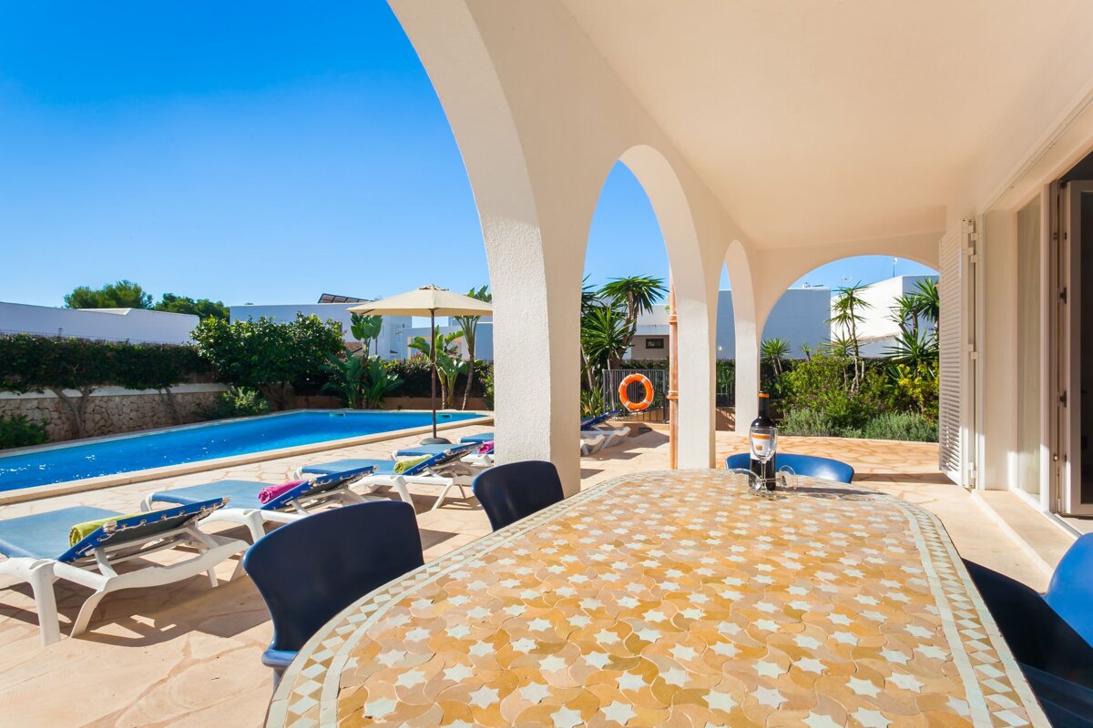 A patio with a table and chairs and a pool in the background