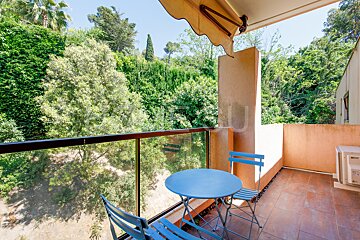 A balcony with a blue table and chairs and trees in the background