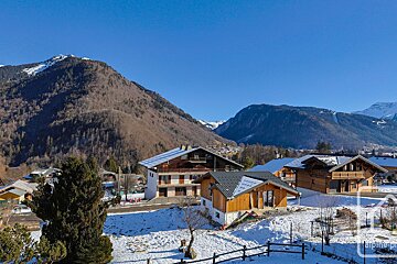 A snowy landscape with a few houses and mountains in the background