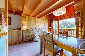 Cozy, wood-paneled chalet interior with a dining table, sofa, and a balcony offering a stunning mountain vista.
