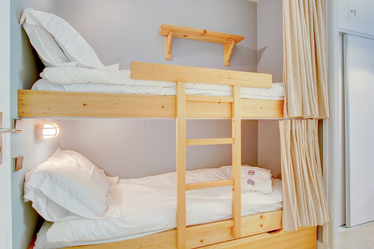 A bunk bed with white sheets and a curtain behind it