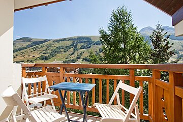 A balcony with two chairs and a table with mountains in the background