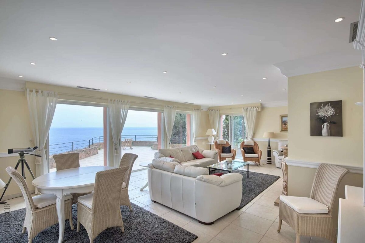 A bright living/dining room with white furniture, ocean-view sliding doors leading to a terrace, and a telescope for stargazing.