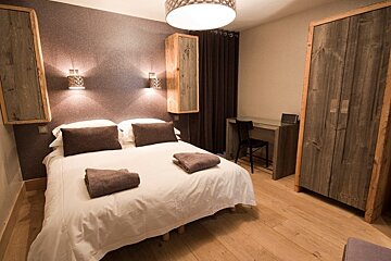 Modern rustic bedroom featuring a double bed with white linens, wooden wardrobe, a desk, and a textured grey accent wall.