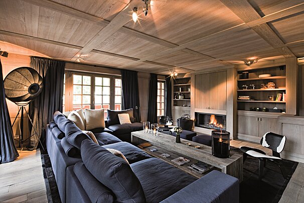 A warm, rustic-modern living room featuring a navy sectional, wood-paneled ceiling, a glowing fireplace, and ambient lighting for a cozy atmosphere.
