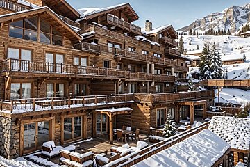 A large multi-level wooden ski resort chalet covered in snow, surrounded by snow-capped mountains.
