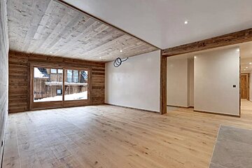 Empty ski chalet room featuring extensive wood paneling, light wood floors, and a glass door with a snowy exterior view.