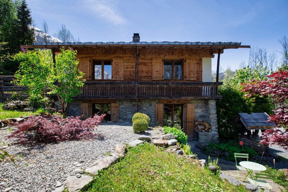 A wooden house with a balcony is surrounded by trees and rocks