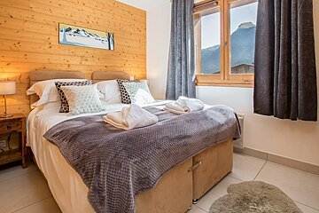 Cozy chalet bedroom featuring a wood-paneled wall, a double bed, and a window with mountain views.