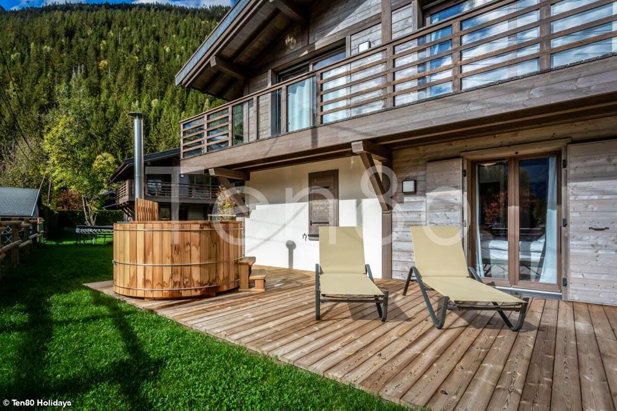 A wooden hot tub sits on the deck of a house