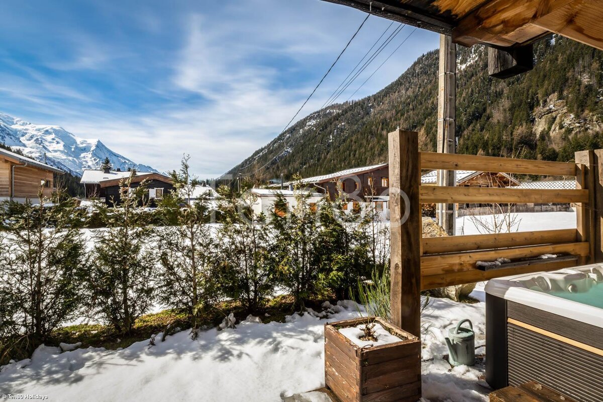 A hot tub sits in front of a wooden fence with mountains in the background