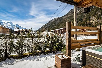 A hot tub sits in front of a wooden fence with mountains in the background