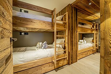 A room with bunk beds made of wood and white sheets