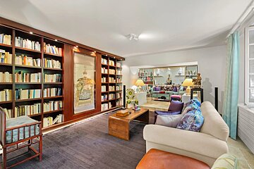 A multi-level living room features a dark wood library wall with a framed art piece, leading to a colorful, eclectic seating area with a sunken section.