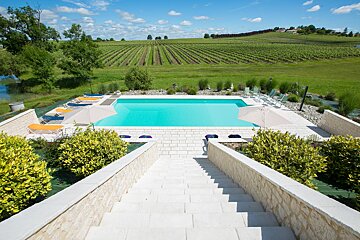 A swimming pool surrounded by chairs and umbrellas with a vineyard in the background