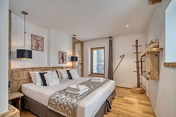 A spacious, rustic-modern bedroom with a king bed, wooden accents, wildlife artwork, a tree-branch coat rack, and light wooden floors.