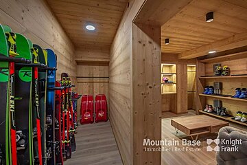 A luxurious wooden ski room with rows of skis, ski boots on shelves, red sleds, and a cozy seating area with a low table.