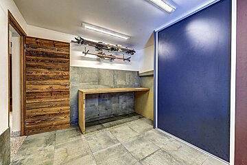 A modern ski room featuring a wooden door, skis stored on wall racks, a wooden bench, tiled floor, and a large dark blue sliding door.