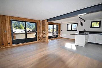 Spacious, modern room featuring wood-paneled walls, large windows with mountain views, light wood floors, and a sleek kitchen island.