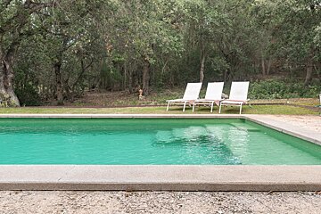 A swimming pool with three white lounge chairs in it