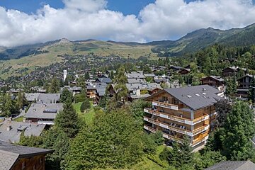 Scenic alpine village with wooden chalets nestled among lush green hills and mountains under a blue sky.