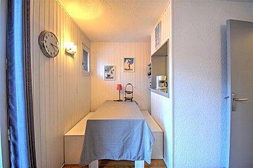 A cozy, brightly lit dining nook with white paneled walls, bench seating, a table, and ski posters. A kitchen pass-through is visible on the right.