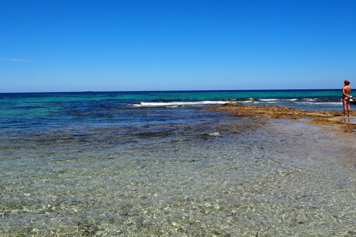 a naked man standing looking out to sea in es cavallet ibiza