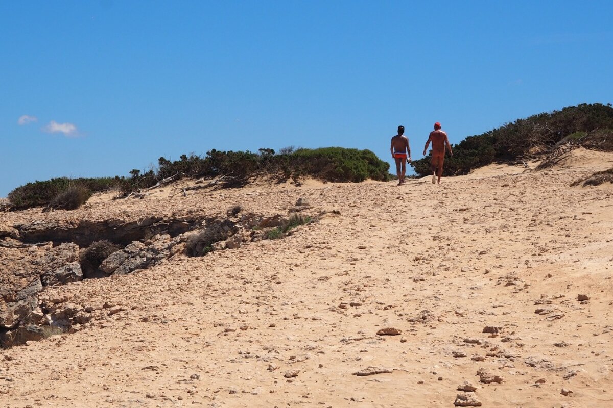 a couple of people hiking in the sand dunes of south ibiza