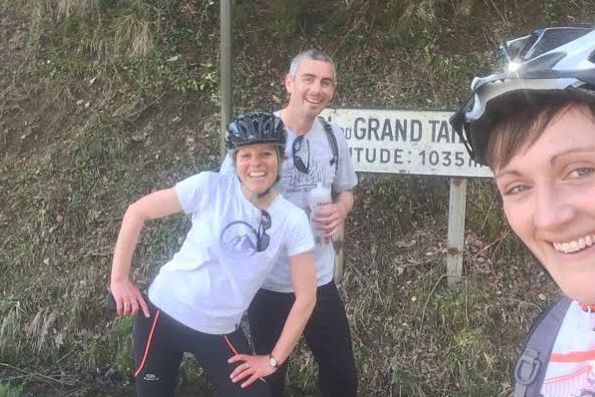 three people by a sign on a road bike climb